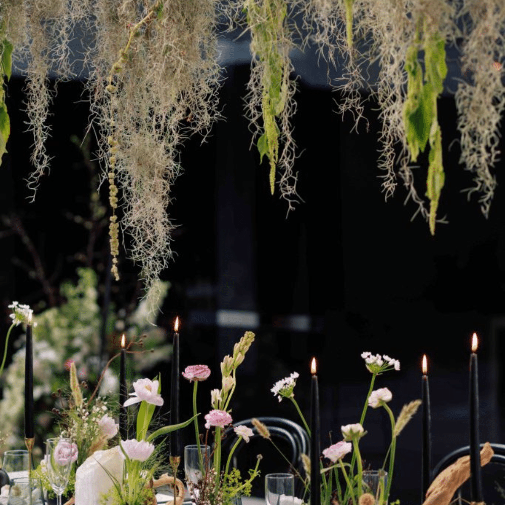 Large greenery installation over eco-conscious wedding tablescape. Featuring black candles and accents, pink florals, and driftwood.