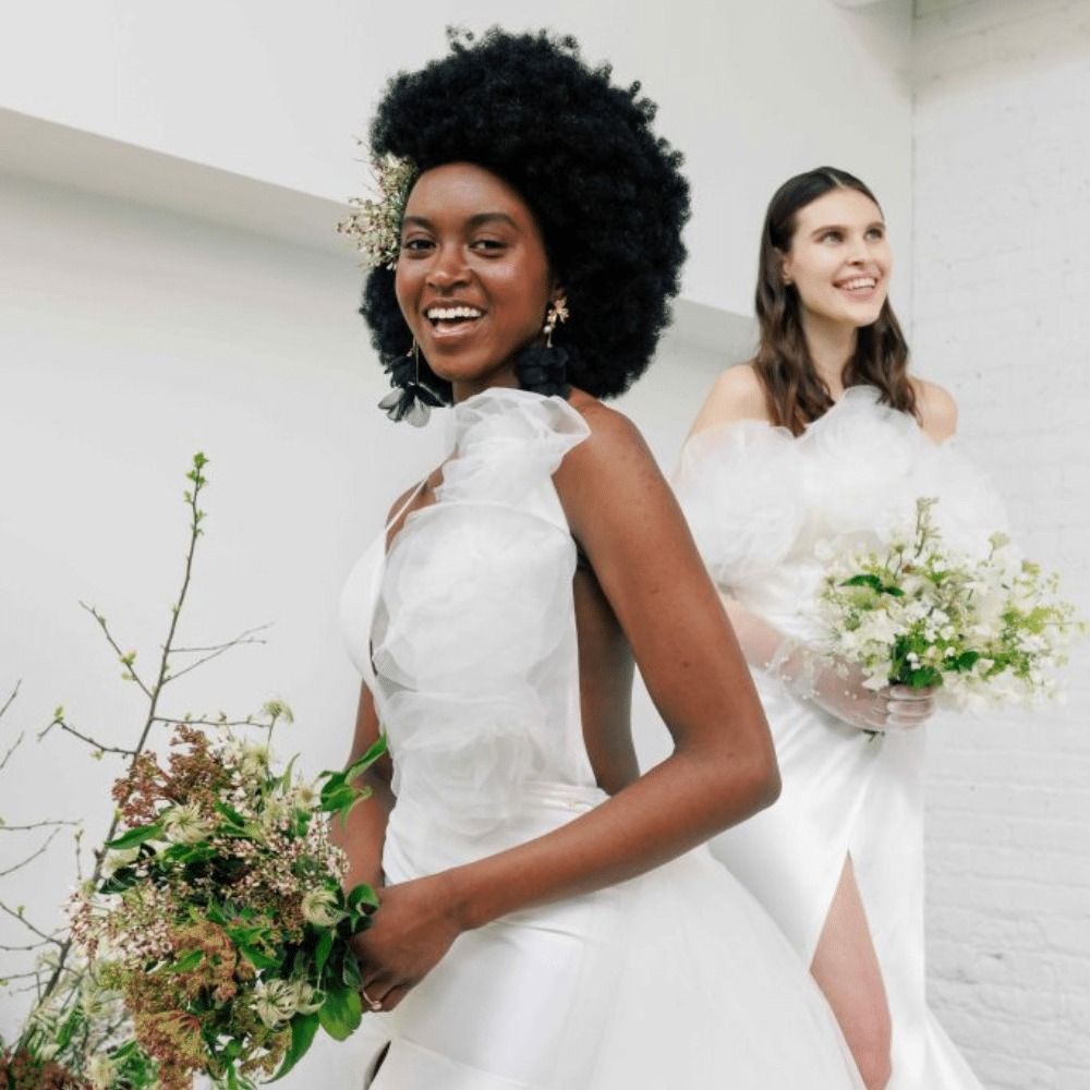 Two brides holding bouquets of white florals and greenery.